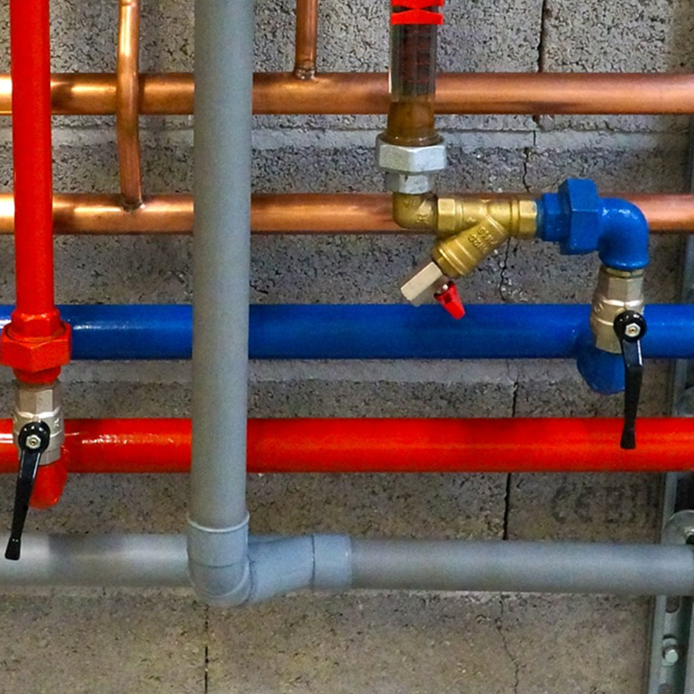 Arco plumbers in Romford. A close up picture of horizontal pipes. Top two are copper, then blue, red and grey.